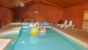 An indoor swimming pool with inflatable toys, lounge chairs, and a wooden ceiling.