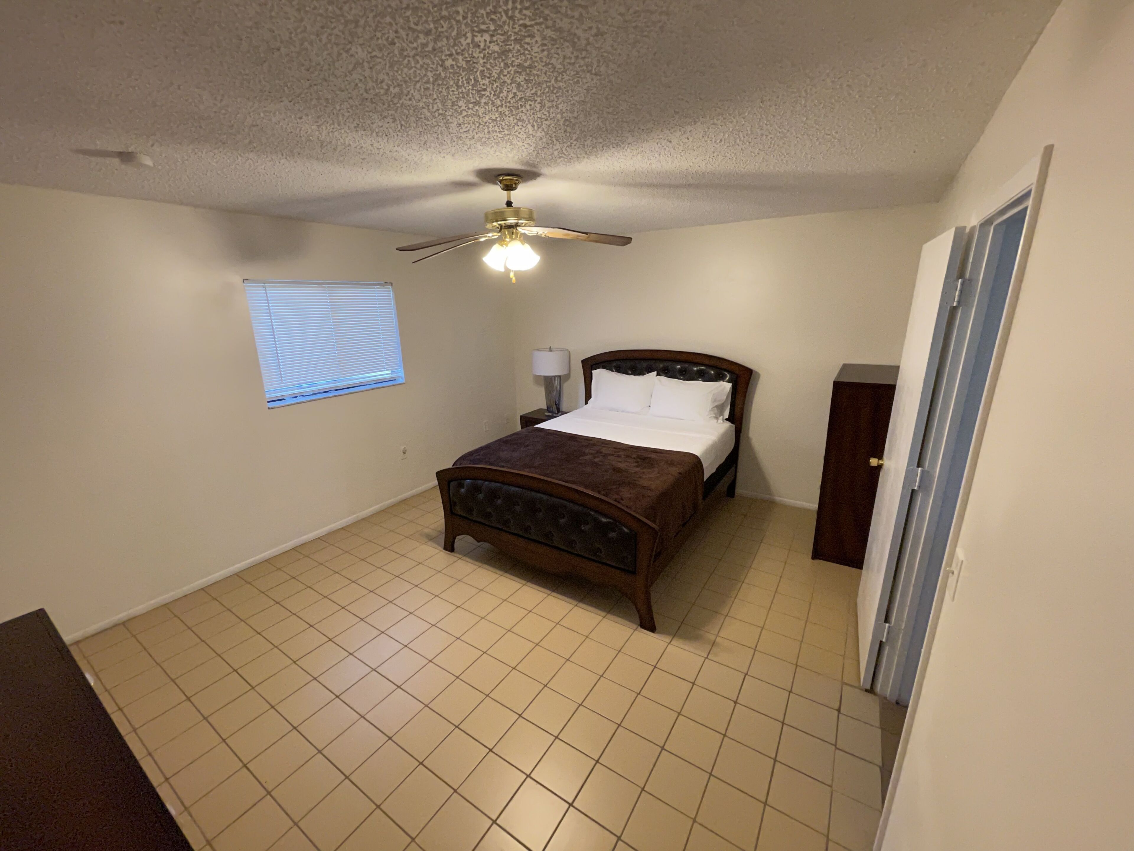 A bedroom with a bed, a ceiling fan, a window with blinds, and a door.