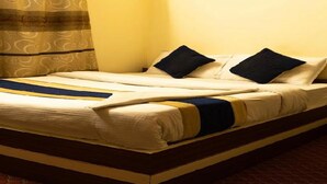 Uma cama bem arrumada com colcha listrada e dois travesseiros, um criado-mudo de madeira e cortinas estampadas.