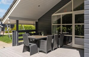 Un patio extérieur couvert, équipé d’une table et de chaises, de grandes fenêtres et d’une balançoire.