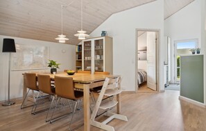 Une cuisine moderne avec une table en bois, des chaises et des luminaires suspendus. On y trouve une bibliothèque avec des portes en verre, donnant sur une autre pièce.