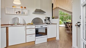 Une cuisine moderne avec des meubles blancs, un four encastré et une machine à café. Une fenêtre offre une vue sur la verdure environnante.
