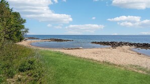 Un paysage côtier comprenant une plage de sable, une côte rocheuse et une zone herbeuse qui descend vers l’eau.
