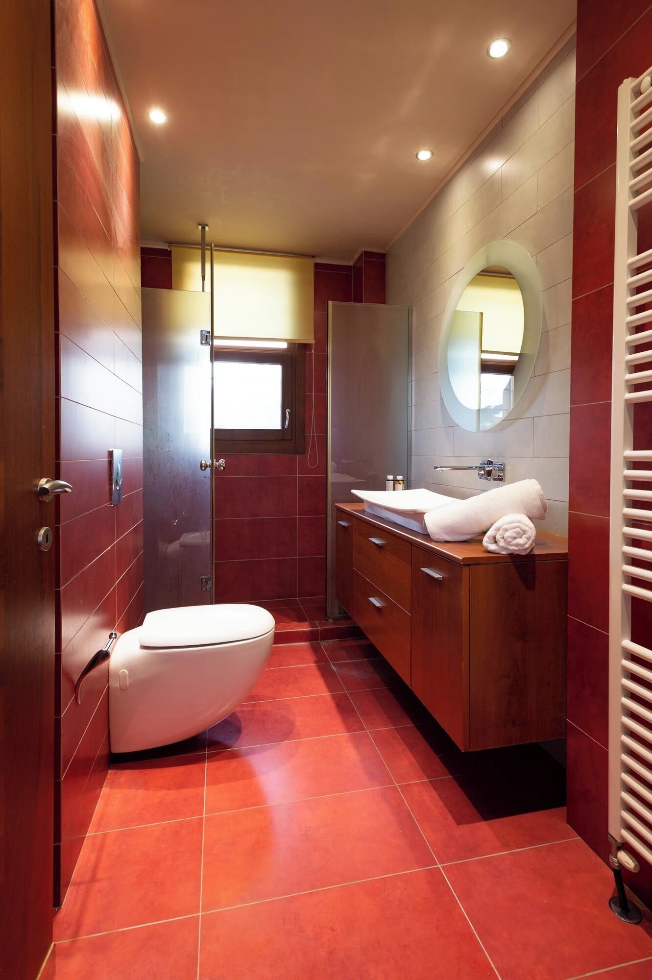 Un bagno compatto con servizi igienici, lavabo e specchio, con pavimento in piastrelle rosse e mobili in legno.
