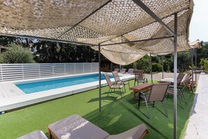 Un espace aménagé au bord de la piscine, avec une pelouse artificielle, des chaises longues et un coin salon abrité.