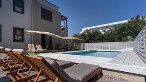A pool area with lounge chairs and umbrellas, surrounded by a white fence and buildings. - Villa Astravi with Private Pool (Ιαλυσός)