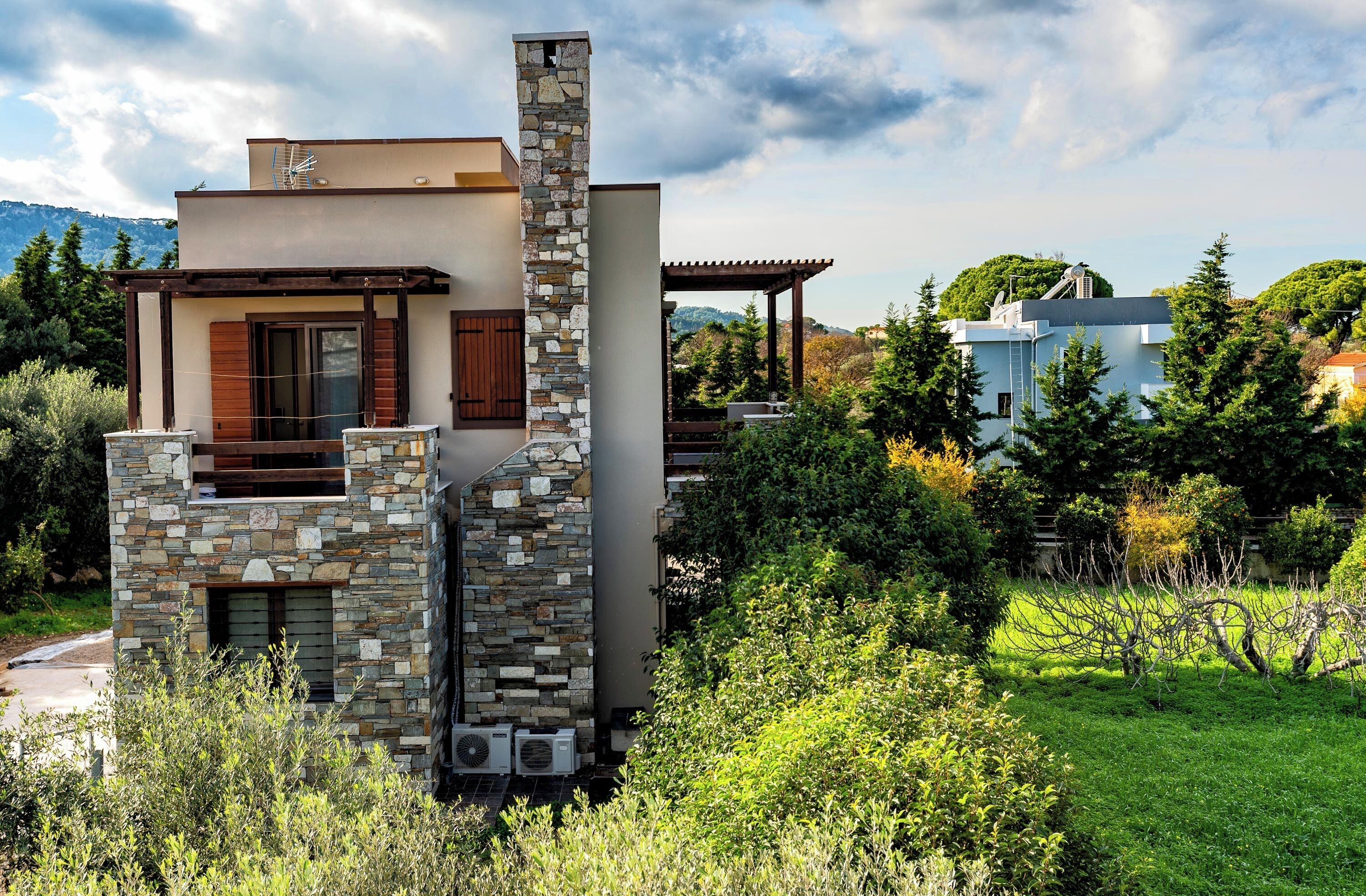 A modern house with a stone facade, a wooden balcony, and a view of the surrounding greenery.