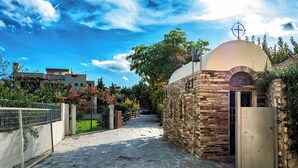 A stone pathway leading to a building with a dome and cross, surrounded by greenery and a clear sky. - Villa Astravi with Private Pool (Ιαλυσός)