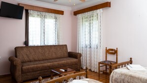 Un salon avec un canapé marron, une chaise en bois, une petite table et un lit recouvert d’une couverture blanche.