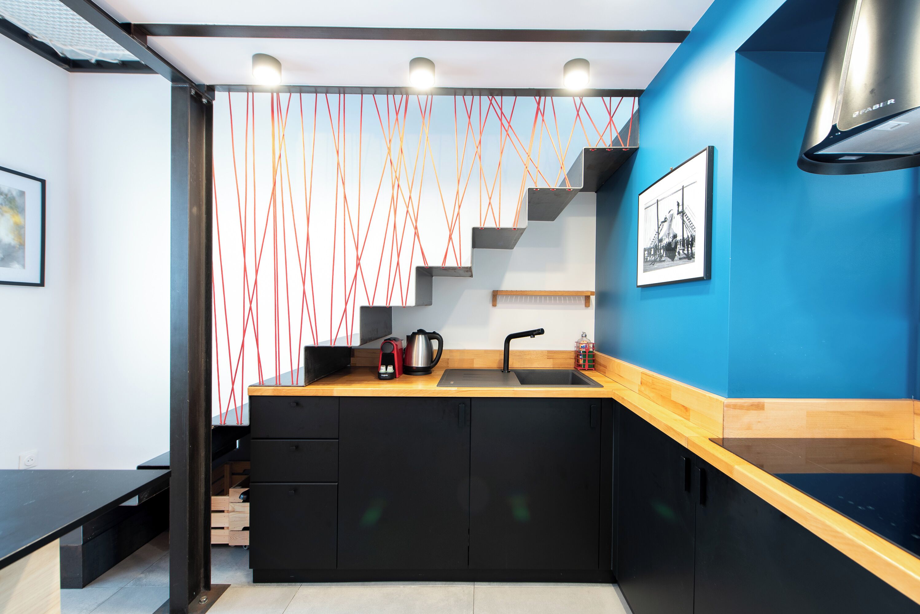 A modern kitchen with a wooden countertop, black cabinets, a stainless steel sink, and a red and white patterned wall.