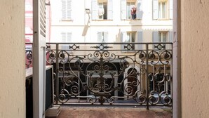 Een balkon met decoratieve smeedijzeren hekwerk, een betegelde vloer en uitzicht op een gebouw met meerdere ramen en luiken.