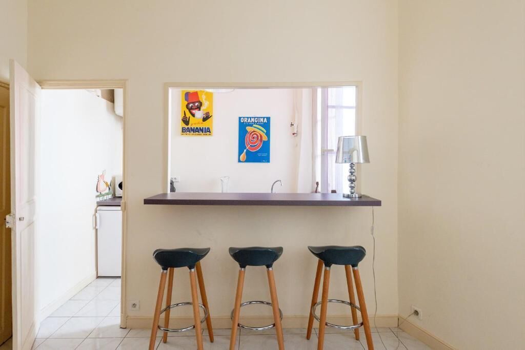 A kitchen with a counter, three stools, and two posters on the wall.