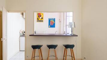 A kitchen with a counter, three stools, and two posters on the wall.