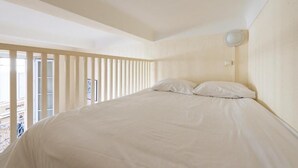 Een slaapkamer met een groot bed, een raam met zonwering en een plafondlamp.