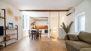 Una sala de estar moderna con suelo de madera, un sofá, un comedor con sillas y una cocina al fondo.