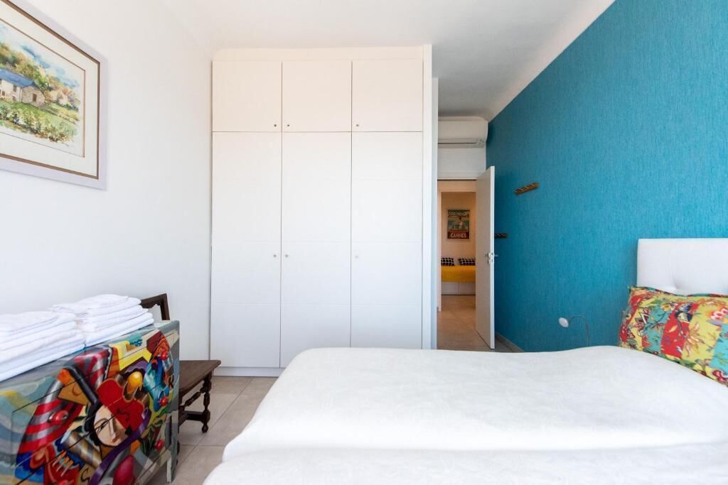 Ein Schlafzimmer mit einem Bett, einem Kleiderschrank, einem Schreibtisch mit farbenfroher Kunst und einer blauen Wand.