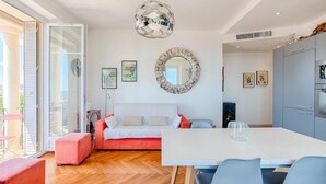 A modern living room with a white sofa, a dining table with chairs, a large mirror, and a unique chandelier. - Le Sinatra splendide vue mer panoramique et balcon (Cannes)