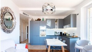 A modern kitchen with blue cabinets, a white dining table, and a unique spherical chandelier. - Le Sinatra splendide vue mer panoramique et balcon (Cannes)