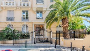 A multi-story building with balconies, a palm tree, and a gated entrance. - Le Sinatra splendide vue mer panoramique et balcon (Cannes)