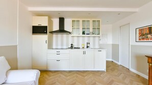Une cuisine de taille réduite avec des meubles blancs, une hotte noire et un four à micro-ondes.