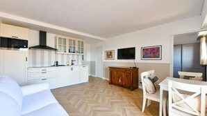 Une cuisine moderne avec des meubles blancs, une hotte noire et un coin repas comprenant une table et des chaises blanches.