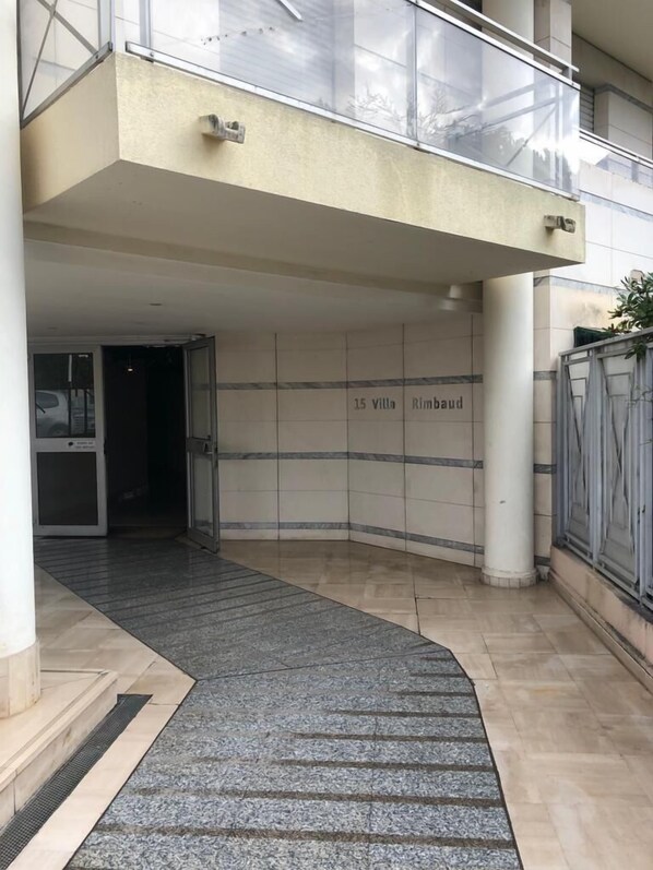A modern building entrance with a tiled wall displaying "15 Villa Rimbaud" and a glass balcony above.