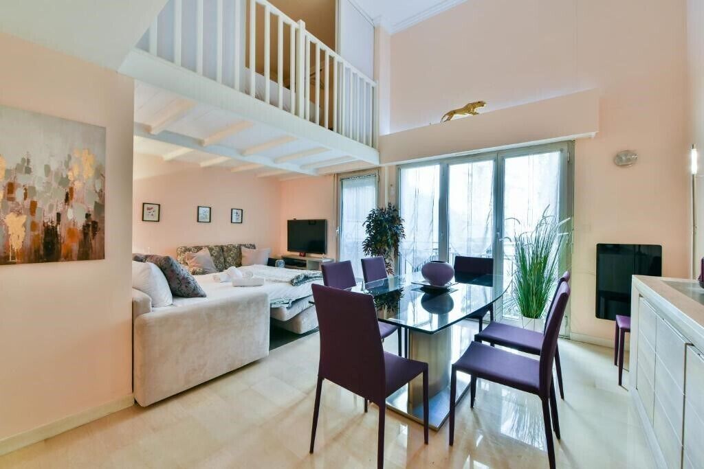 A modern living space with a dining area, a sofa set, a staircase, and a large window providing natural light.