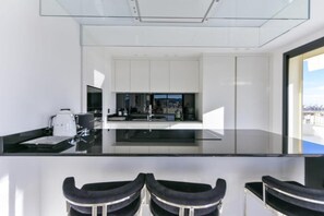 A modern kitchen with a glass countertop, white cabinets, and a view of the city. - L'Horizon avec somptueuse terrasse vue mer (Cannes)