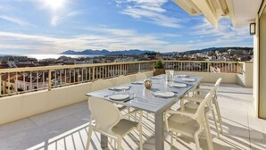 A balcony with a table set for dining, overlooking a cityscape with mountains in the distance. - L'Horizon avec somptueuse terrasse vue mer (Cannes)