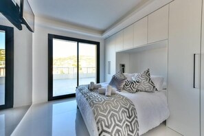 A modern bedroom with a large bed, a sliding glass door to a balcony, and built-in white wardrobes. - L'Horizon avec somptueuse terrasse vue mer (Cannes)