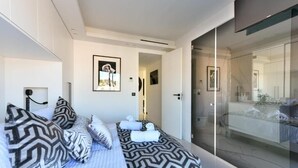 A modern bedroom with a bed, patterned pillows, and a glass shower area. - L'Horizon avec somptueuse terrasse vue mer (Cannes)