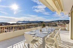 A balcony with a table set for dining, overlooking a cityscape with mountains in the distance. - L'Horizon avec somptueuse terrasse vue mer (Cannes)
