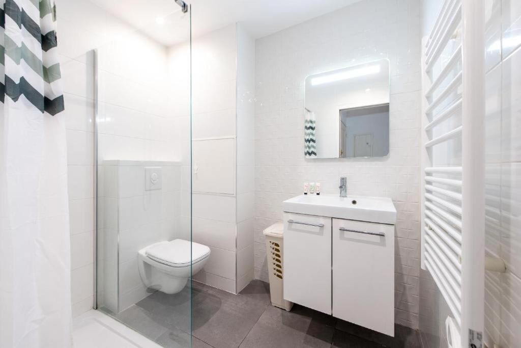 Een moderne badkamer met een glazen douchecabine, een wit toilet en een witte wastafel met spiegel.