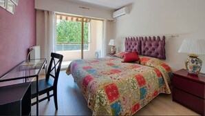 A bedroom with a bed, a desk, a chair, a window with a view of greenery, and a ceiling light.