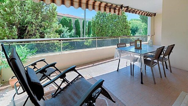 A balcony with a glass table and chairs, a view of trees, and a striped awning.