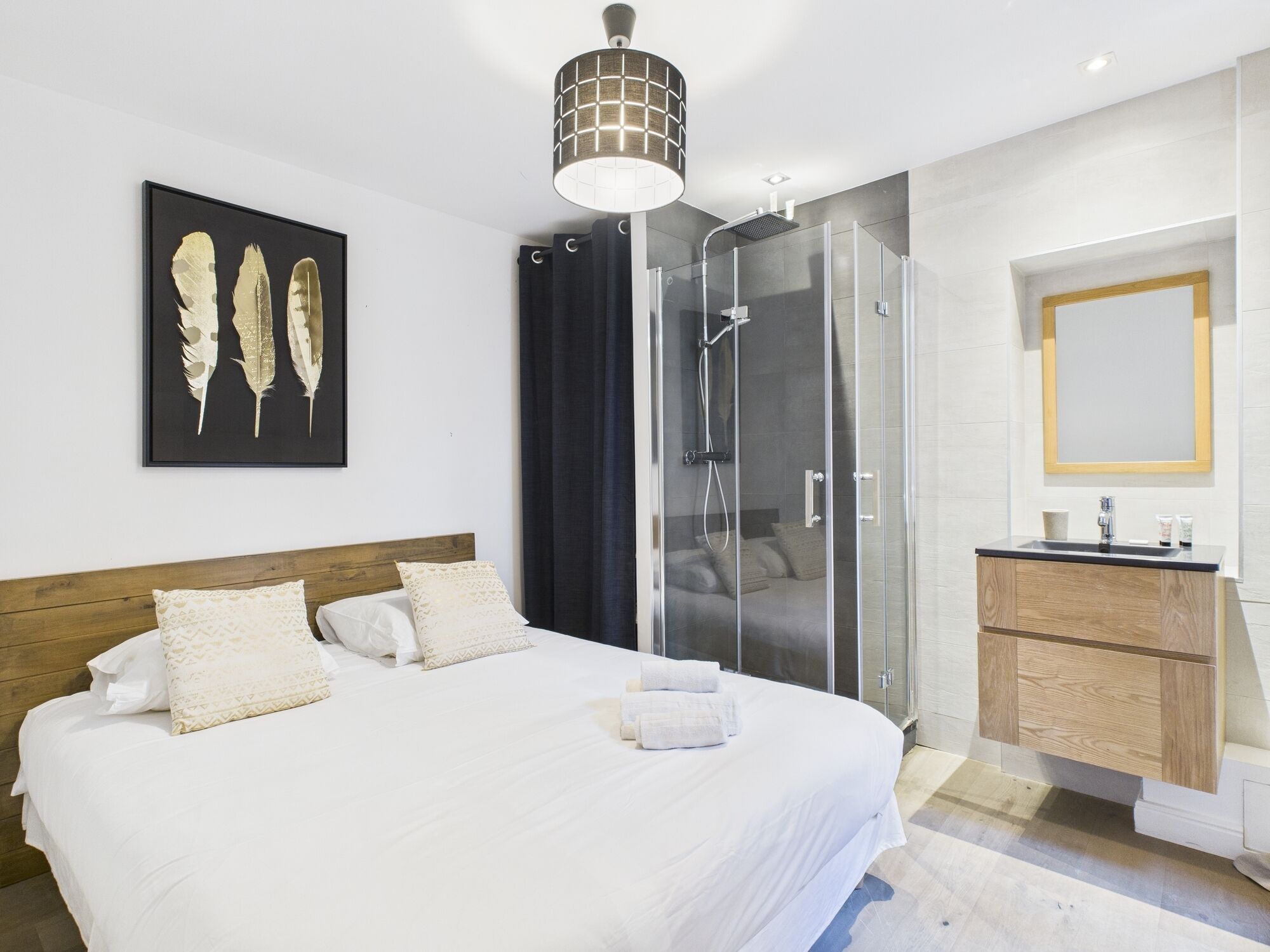 Camera da letto moderna con un ampio letto, cabina doccia in vetro, testiera in legno e un'opera d'arte incorniciata appesa al muro.