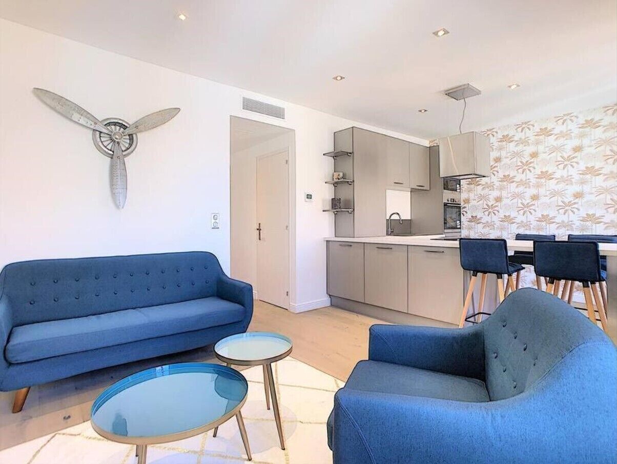 A modern living room with a blue sofa, a glass coffee table, and a dining area with a white table and chairs.