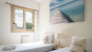 Habitación de hotel con dos camas, una ventana, un radiador, un cuadro de un muelle y una almohada con la palabra 'Cannes'.