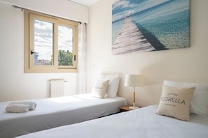 Habitación de hotel con dos camas, una ventana, un radiador, un cuadro de un muelle y una almohada con la palabra 'Cannes'.