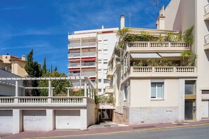 A multi-story building with balconies, a gated entrance, and a clear sky.