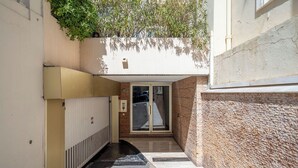 Un callejón estrecho con una puerta que da a un edificio, un radiador a la izquierda y una pared texturizada a la derecha.