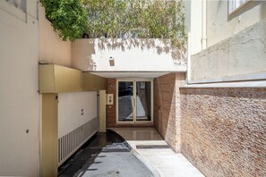 A narrow alleyway with a door leading to a building, a radiator on the left, and a textured wall on the right. - Le Corail spacieux avec beau et ample balcon (Cannes)