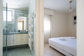 Habitación de hotel con cama, baño con cabina de ducha de vidrio y vistas al exterior.