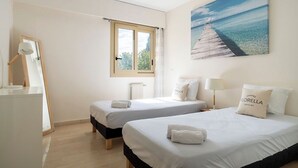 Hotelkamer met twee bedden, een raam, een schilderij van een pier, een bureau met lamp en een radiator.