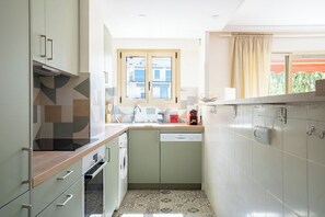 Una cocina compacta con lavavajillas, una ventana con vista a edificios y un piso estampado.