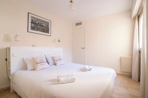 A bedroom with a bed, pillows, a framed picture, a radiator, and a window with curtains. - Le Corail spacieux avec beau et ample balcon (Cannes)