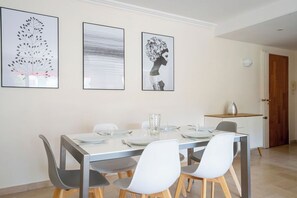 A dining area with a rectangular table, four chairs, and three framed artworks on the wall.