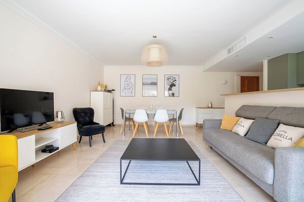 A modern living room with a flat-screen TV, a sofa, a dining table with chairs, and artwork on the wall.