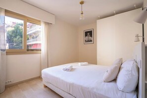 A bedroom with a bed, a window, a picture on the wall, and a ceiling light.