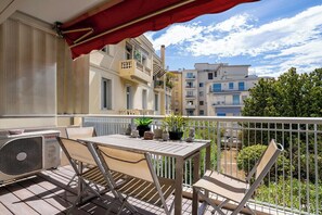 A balcony with a table and chairs, a red awning, and a view of neighboring buildings.